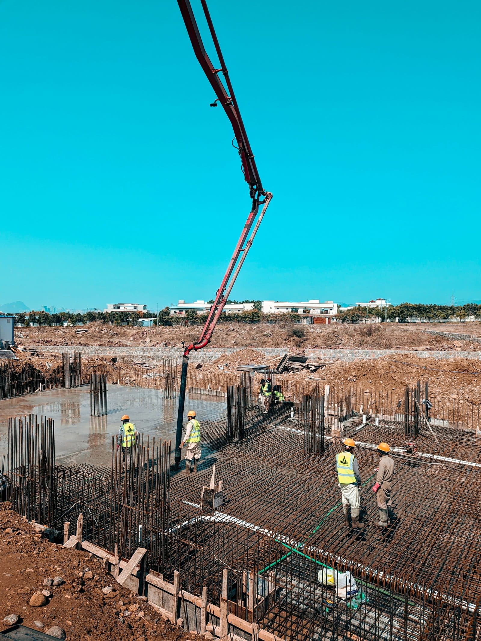 A concrete pump boom placing concrete over a reinforced foundation raft while site crew guide the pour.