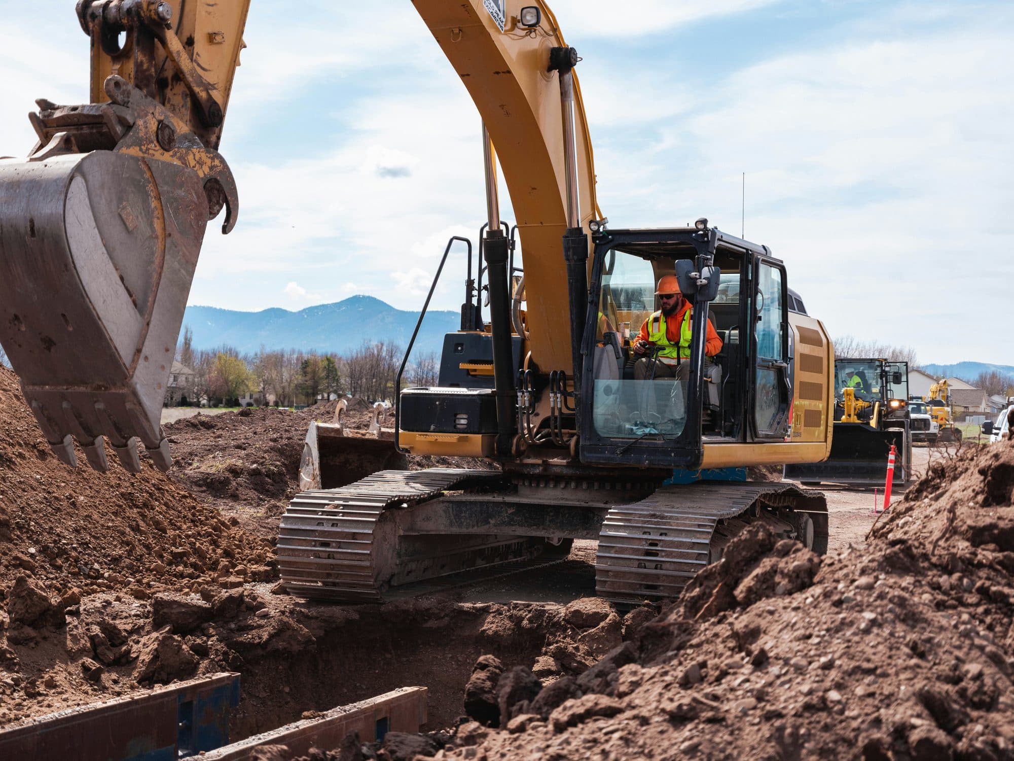 A tracked excavator cutting into a red-soil embankment during bulk earthworks, with the operator at the controls.