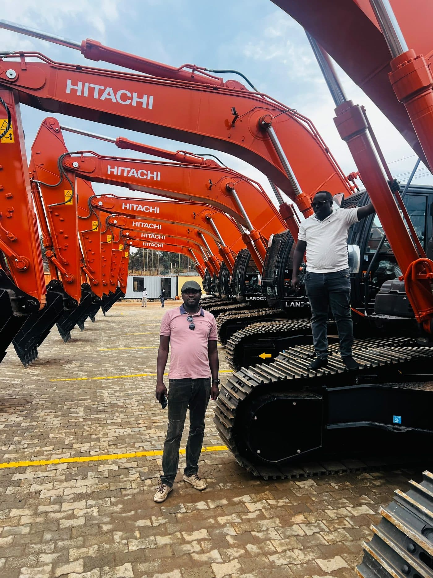 A line of tracked excavators parked in a yard ahead of deployment, with personnel alongside.